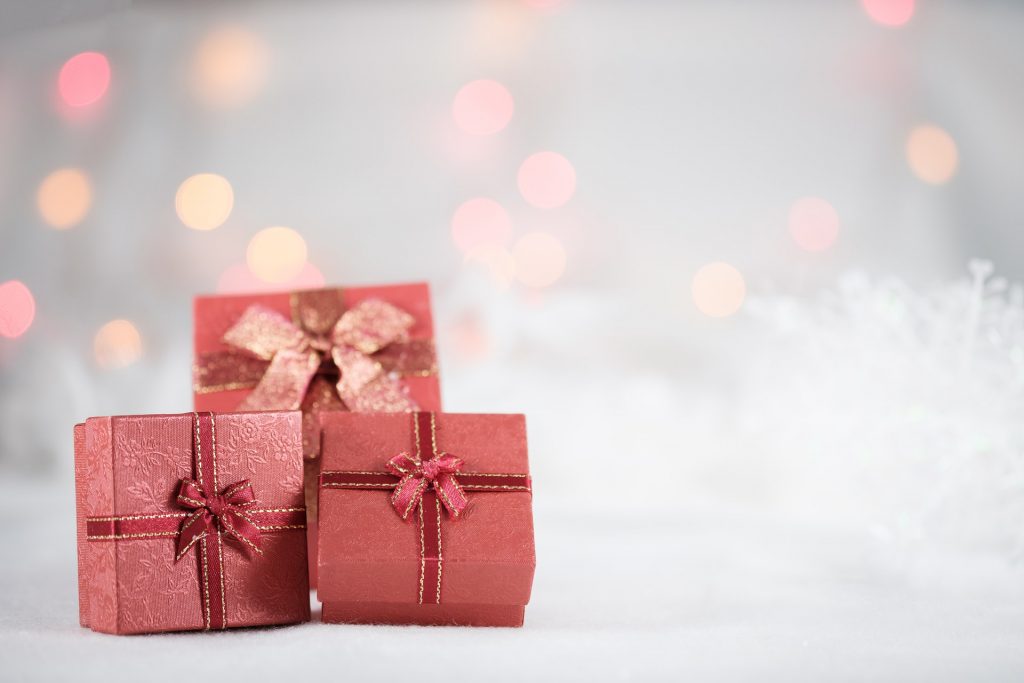 A thoughtful gift starts with the person wearing it. Red wrapped Christmas gift boxes beside soft holiday lights