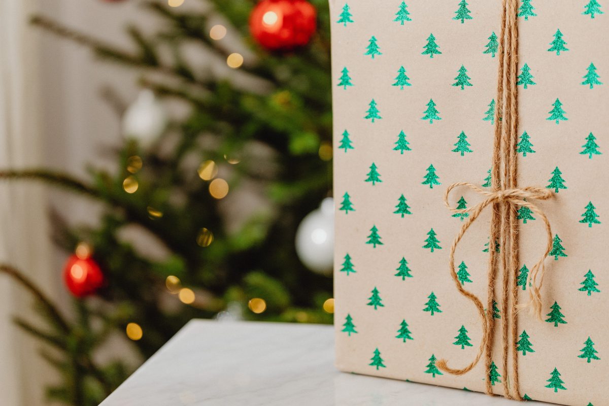 A wrapped gift tied with string beside a decorated Christmas tree