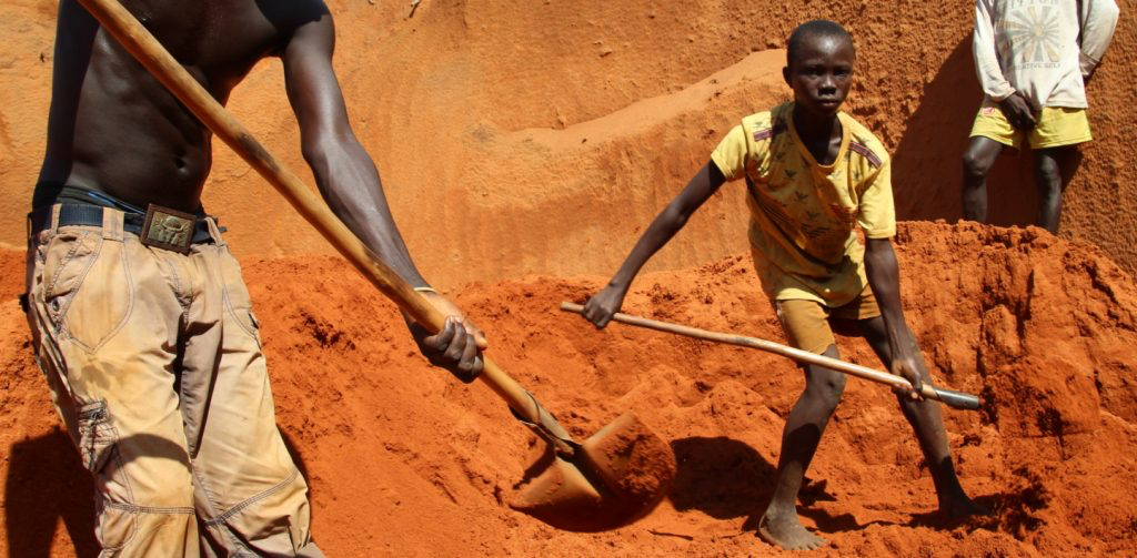 People digging with shovels in an open red-earth pit