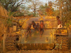Armed figures beside an armored vehicle in a wooded area
