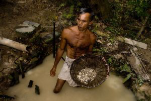Miner standing in water with a basket of excavated gravel