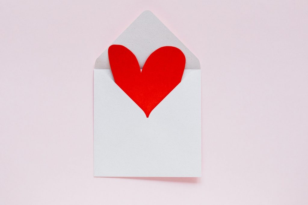 A red paper heart inside a white envelope on a pink background