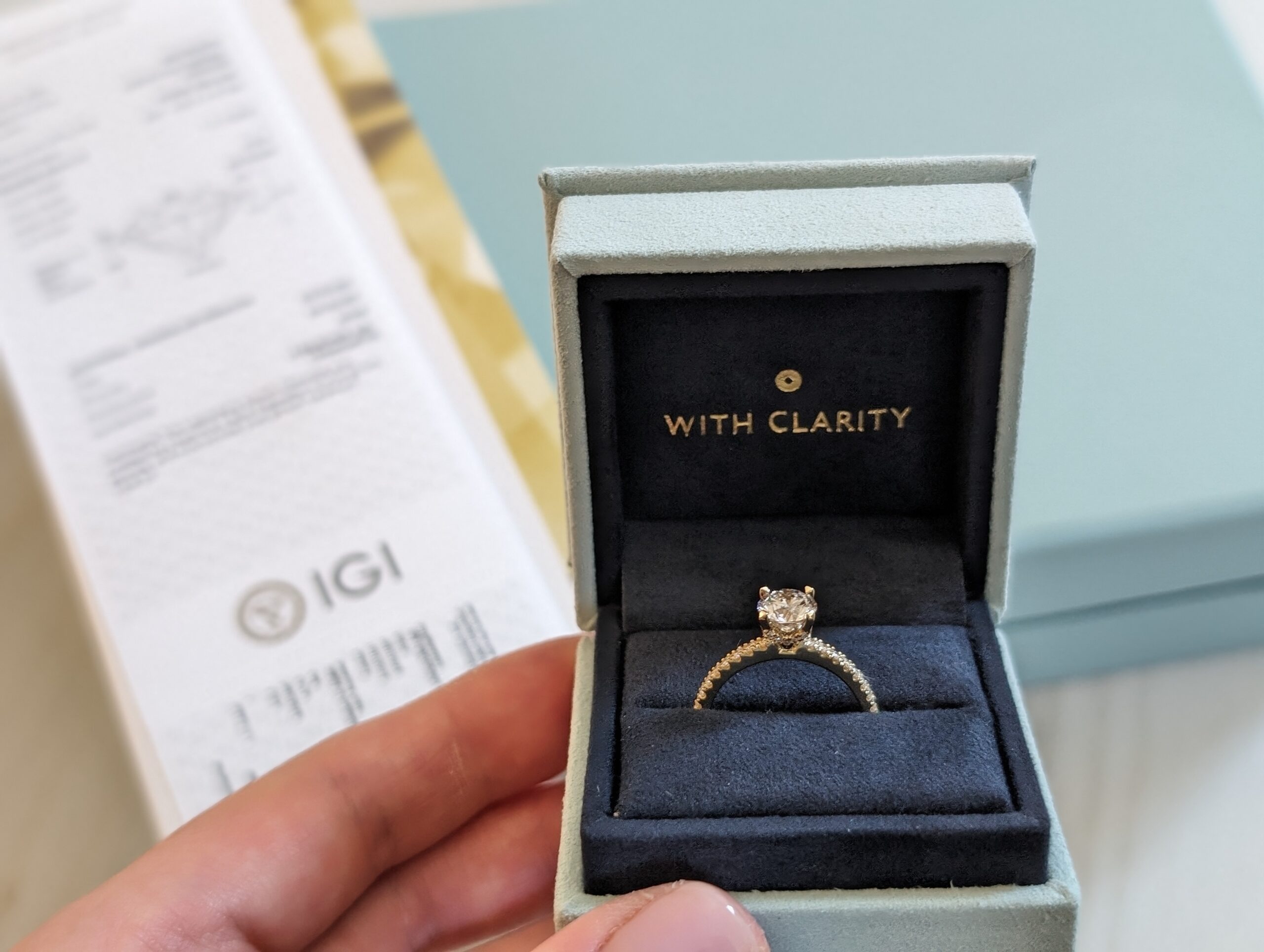 Our Chevron Hidden Halo ring in its blue With Clarity presentation box. With Clarity ring shown in its open presentation box