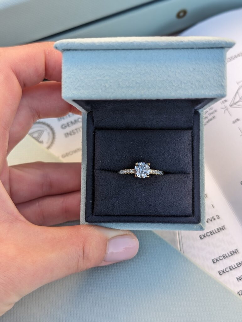 1.11 carat round lab-grown diamond engagement ring from With Clarity shown inside blue jewelry box.